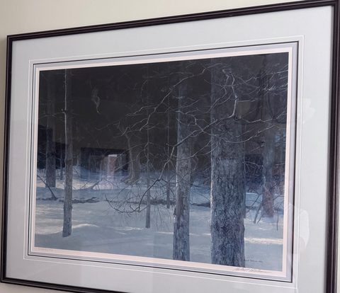 A framed Robert Bateman print of bare trees in snow, hanging on a wall.