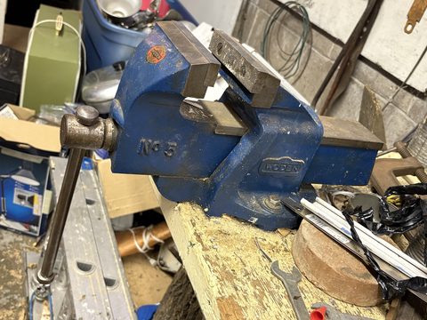 A blue Record No 5 bench vise clamped to a workbench in a full garage.