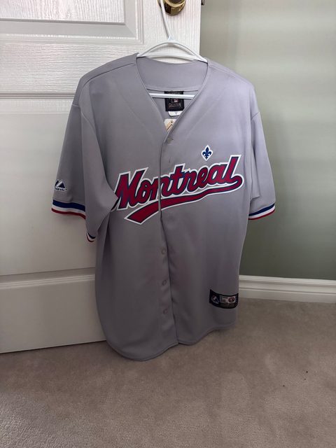A grey Montreal Expos baseball jersey hanging on a door, new with the tag on.