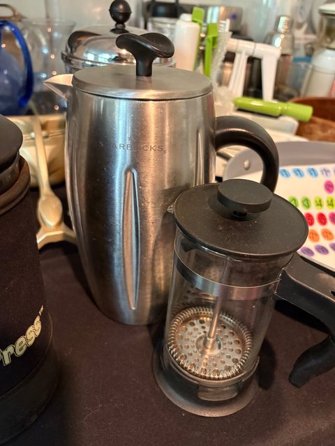 A stainless steel thermal jug and a glass cafetière on a table of kitchenware.