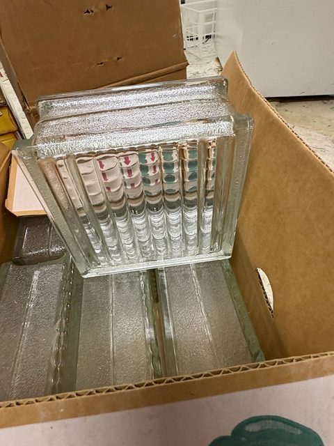 A cardboard box of pressed glass dishes stacked on their sides.