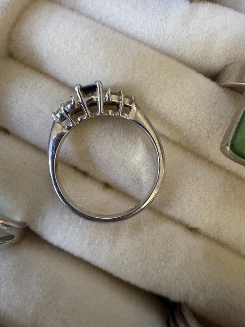 A white gold ring set with a dark blue stone and small diamonds, resting on a cushion.